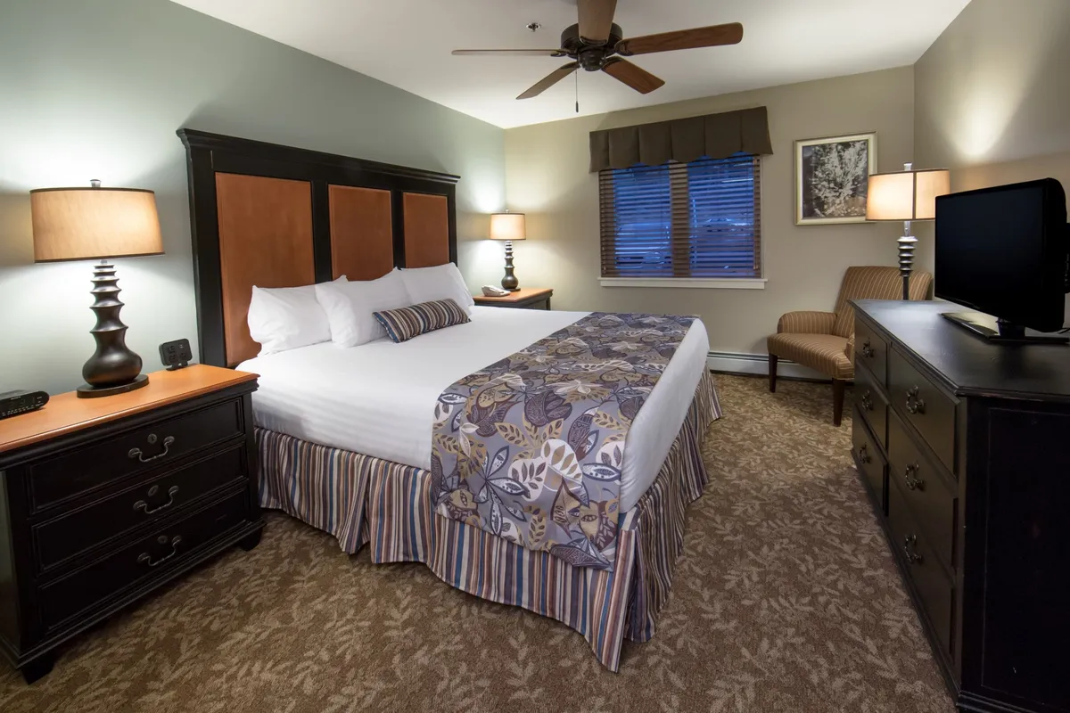A welcoming villa bedroom featuring a comfortable bed, nightstands, a dressing chair, and a flatscreen television. The mood is soft and inviting, with personal touches like a cozy chair for reading and the TV for entertainment, suggesting a space designed for restful moments and connectivity.