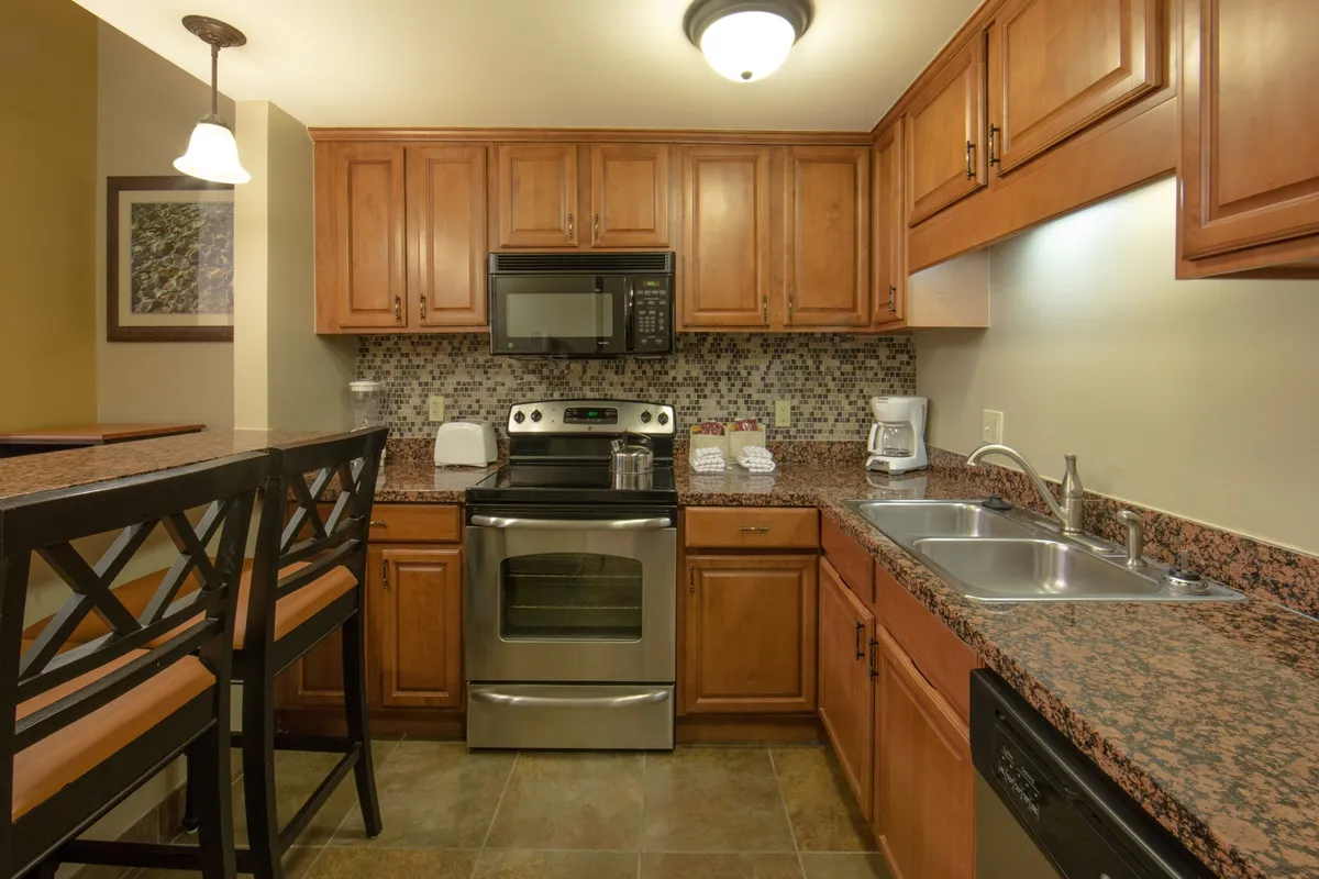 This image features the kitchen area with stylish cabinetry, stainless steel appliances, granite countertops, and bar seating. The layout shows a space ready for cooking and entertaining, equipped with modern amenities and a welcoming atmosphere for both quick meals and more elaborate culinary endeavors.