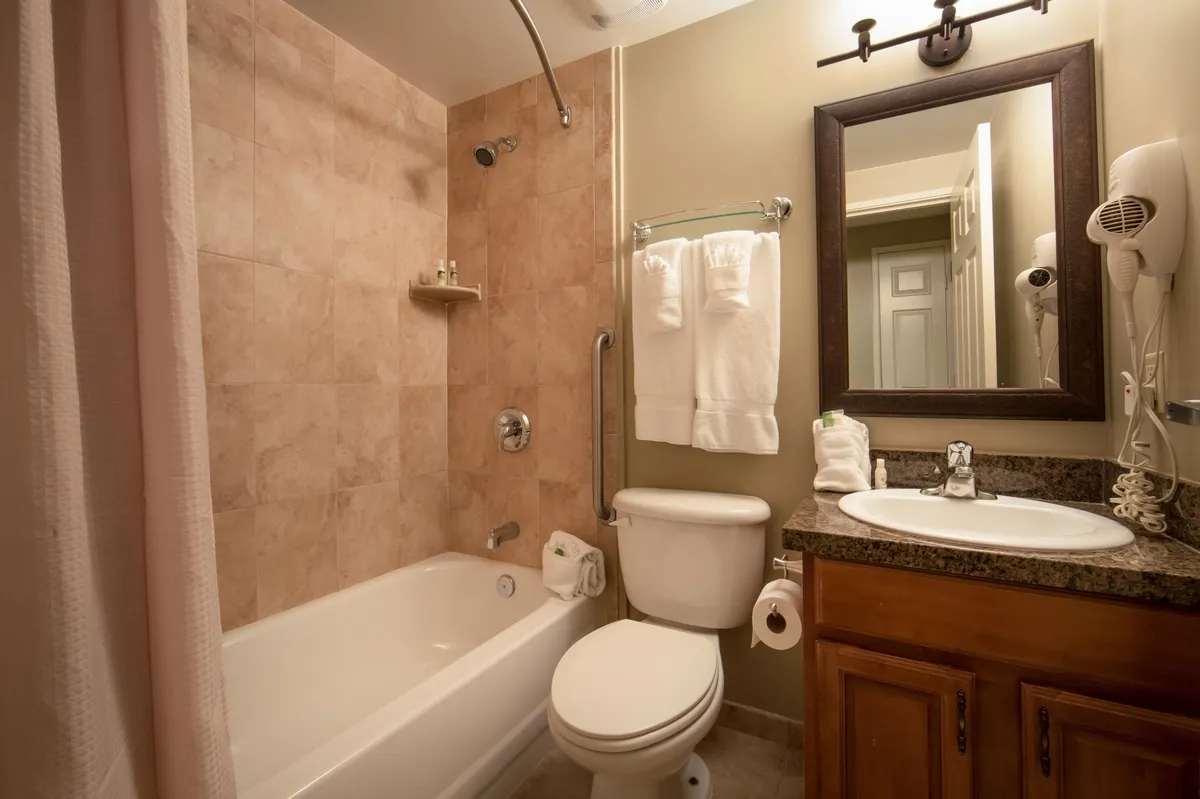 A calming bathroom interior featuring a modern bathtub, sleek sink, and large mirror. Soft lighting enhances the soothing atmosphere, and fluffy towels are neatly arranged, hinting at spa-like comforts. Subtle accents and clean lines contribute to a sense of relaxation and rejuvenation.