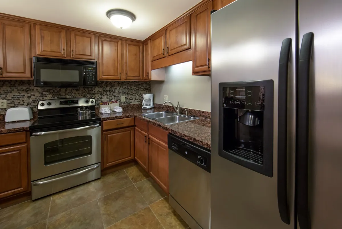 The image showcases a beautifully appointed kitchen with stainless steel appliances, granite countertops, rich wood cabinetry, and a stylish mosaic backsplash. The space is warm and inviting, ideal for cooking, baking, and spending quality time together.